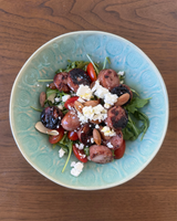 A bowl of Chicken Sausage Salad featuring grilled sausage, cherry tomatoes, arugula, feta, almonds, and a drizzle of olive oil.