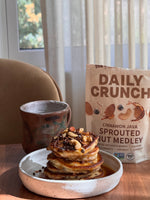A stack of pancakes drizzled with syrup and topped with Daily Crunch Cinnamon Java Sprouted Nut Medley