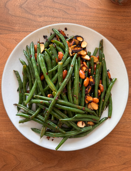 A plate of green beans with almonds on top. 