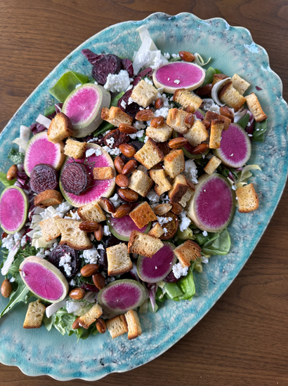 A vibrant salad with sliced watermelon radishes, beets, croutons, almonds, and crumbled cheese