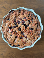 A freshly baked almond and berry crumble in a round, scalloped-edge baking dish.