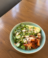 A bowl of mixed vegetables, including cucumbers, avocado, and greens, topped with sliced almonds and sesame seeds.