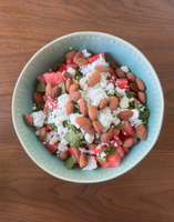 A bowl of watermelon cubes topped with feta cheese, almonds, and mint leaves