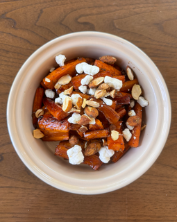 A bowl of roasted carrots topped with crumbled goat cheese and sliced almonds.