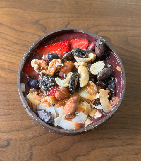 A smoothie bowl topped with mixed nuts, dried fruit, coconut flakes, and fresh berries, served in a coconut shell bowl