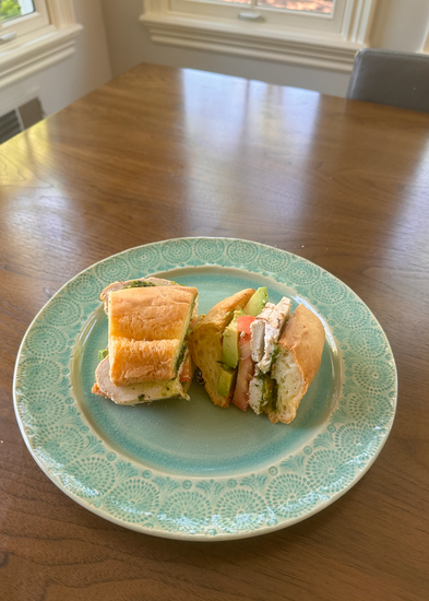 A sandwich with chicken, avocado, tomato, and greens on a turquoise plate