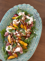 A salad with fresh greens, sliced peaches, prosciutto, burrata, almonds, and mint leaves.